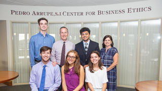 A group of students and faculty smile in front of the arrupe sign